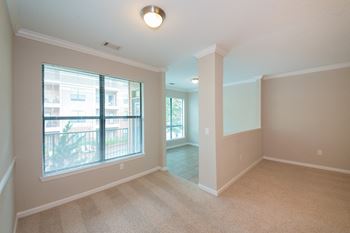 A room with a carpet floor, a window with blinds, and a balcony outside.